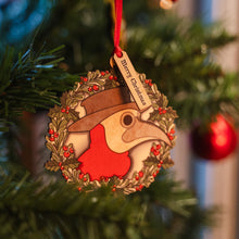 Load image into Gallery viewer, A wooden wreath hanging decoration on a Christmas tree, featuring the head of the Plague Doctor at The Real Mary King's Close