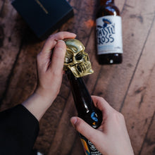 Load image into Gallery viewer, Gold skull bottle opener being used to open a beer
