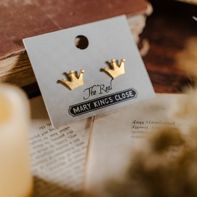 Simple three-pronged gold crown stud earrings on a label with The Real Mary King's Close branding