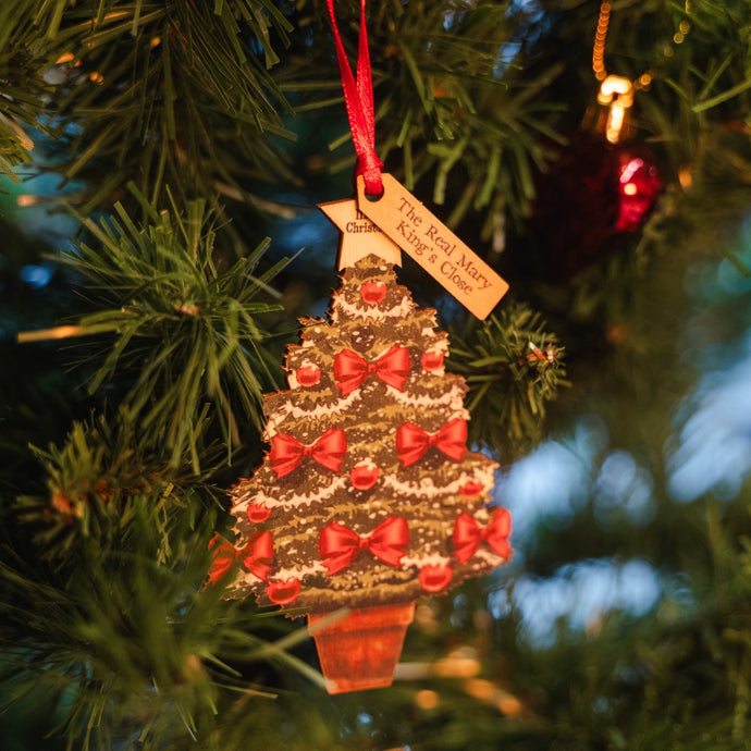A wooden Christmas tree decoration hanging on a tree with a label that reads 