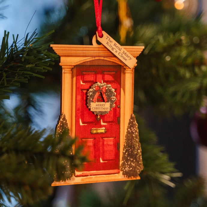 Red door with wreath wooden decoration hanging on a Christmas tree, labelled with a message reading 