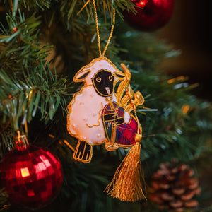 Hand-stitched bagpiping sheep decoration hanging on a Christmas tree with a large, gold tassel 