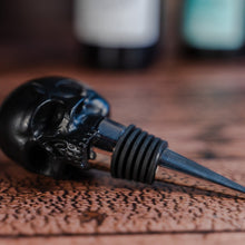 Load image into Gallery viewer, Black skull wine stopper laid on a wooden table
