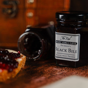 An open jar of blackcurrant preserve labelled "black bile" sitting on its side