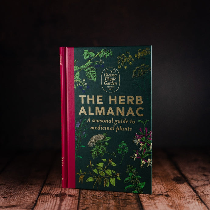The Herb Almanac by Chelsea Physic Garden front cover displayed on a wooden slatted table