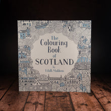 Load image into Gallery viewer, The Colouring Book of Scotland displayed on a wood panelled desk 
