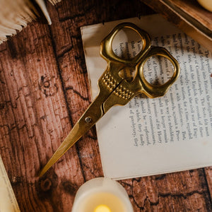 Top view of golden skull scissors set against a wooden table and page of a book