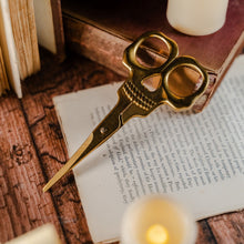 Load image into Gallery viewer, Gold skull scissors against a wooden table and weathered book
