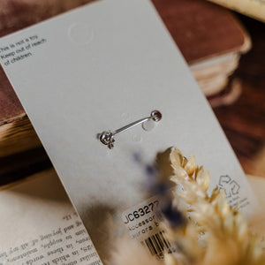 Back of jewellery packaging with a security pin, displayed against dried flowers and a book